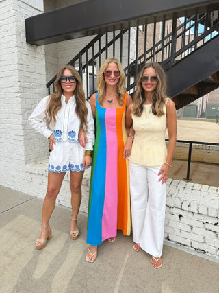 Three women posing together outdoors, wearing stylish outfits.