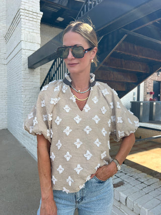 Woman wearing a beige floral blouse and sunglasses outdoors.